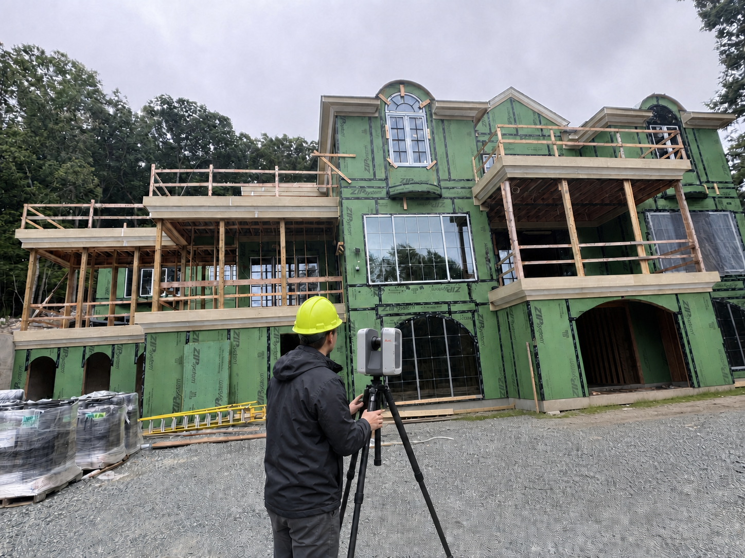 Professional surveyor in a yellow hardhat using a grey-and-white tripod-mounted Leica RTC360 laser scanner to capture a building façade